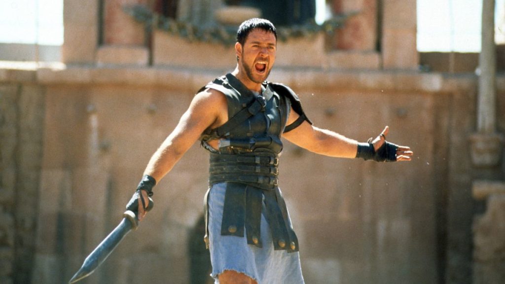 The protagonist of Gladiator, Maximus, wields his gladius and postures in front of a crowd.
