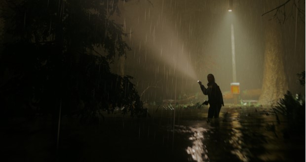 A screencap from the game "Alan Wake 2", where one of the playable characters is standing in the rain with their flashlight, looking around.