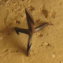 A partially rusted caltrop sits on a stone surface.