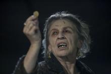 An old woman holds a coin in the air as part of a curse