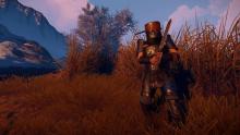 A heavily armored Rust player crouches near some tall grass.